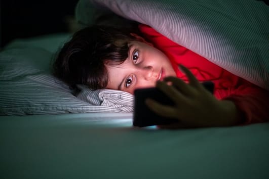 boy lying on bed holding smartphone